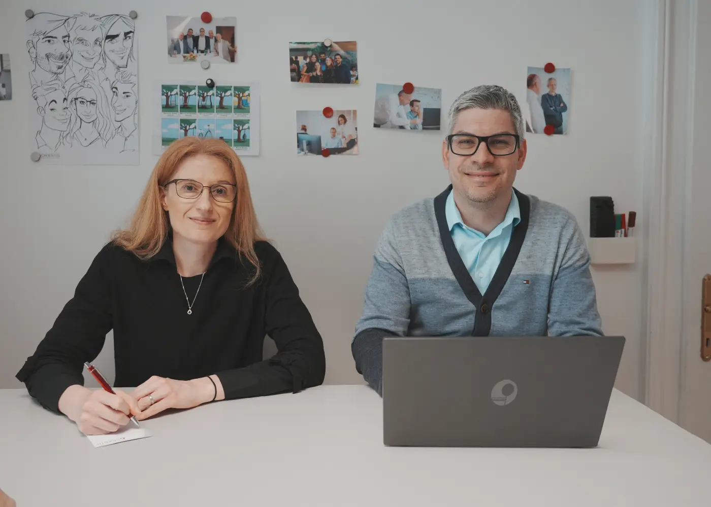 Zwei Objentis Mitarbeiterinnen schauen lächelnd in die Kamera. Vor ihnen steht ein aufgeklappter Laptop und über ihnen schwebt das Objentis Logo.